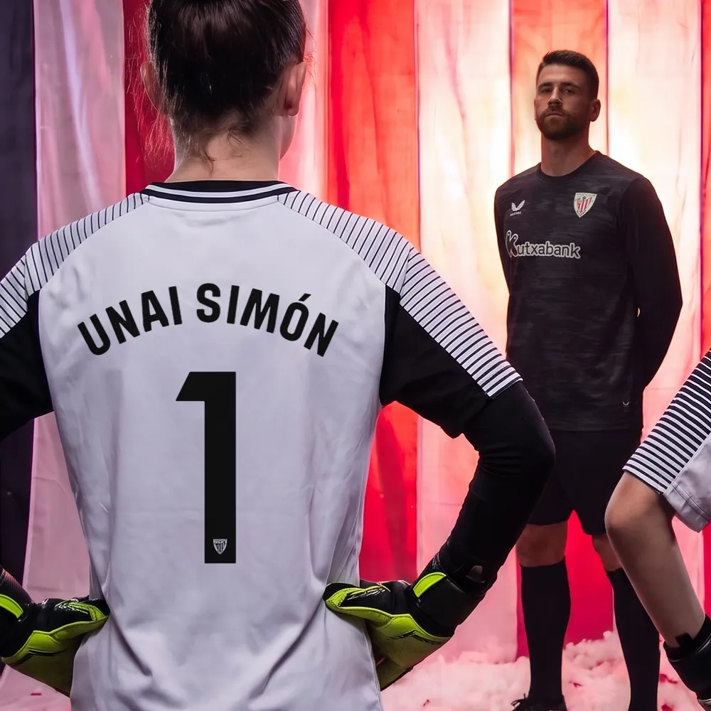 Una portera de AC Campus de espaldas, con la camiseta blanca y el dorsal 1 de Unai Simón; al fondo, Unai Simón